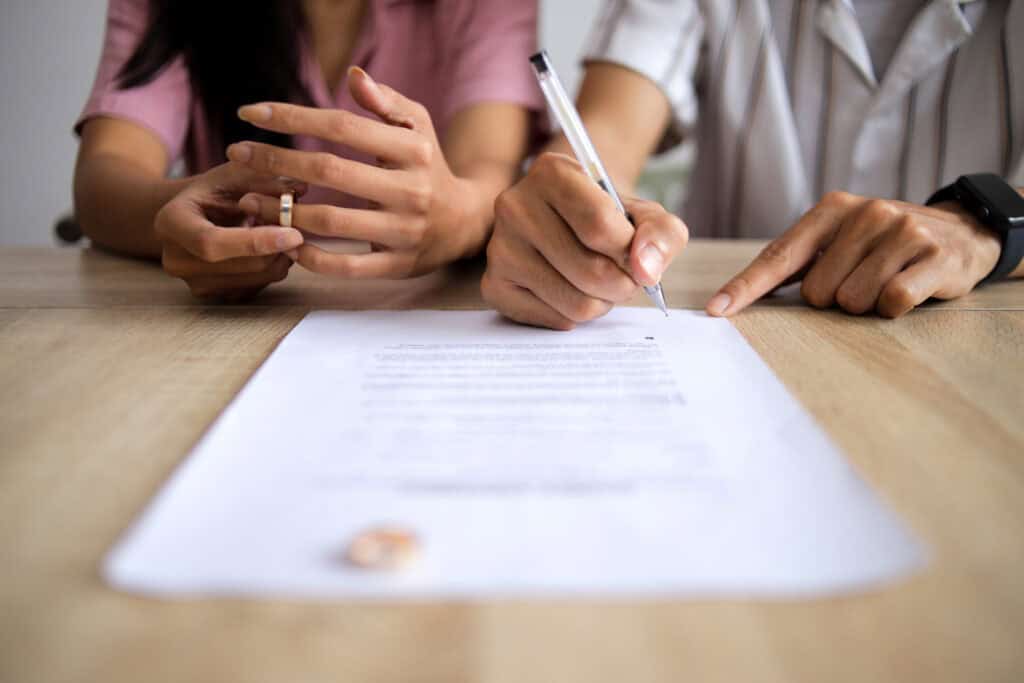 Man Hand Signing Legal Divorce Documents, Deal or Paper Contract in Lawyer Office with Ring Placed on Table